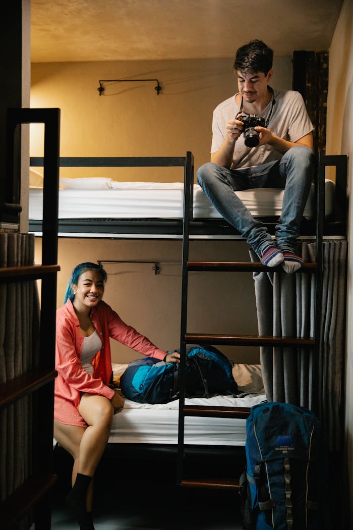 Home Two young travelers enjoying their hostel stay with bunk beds and backpacks.