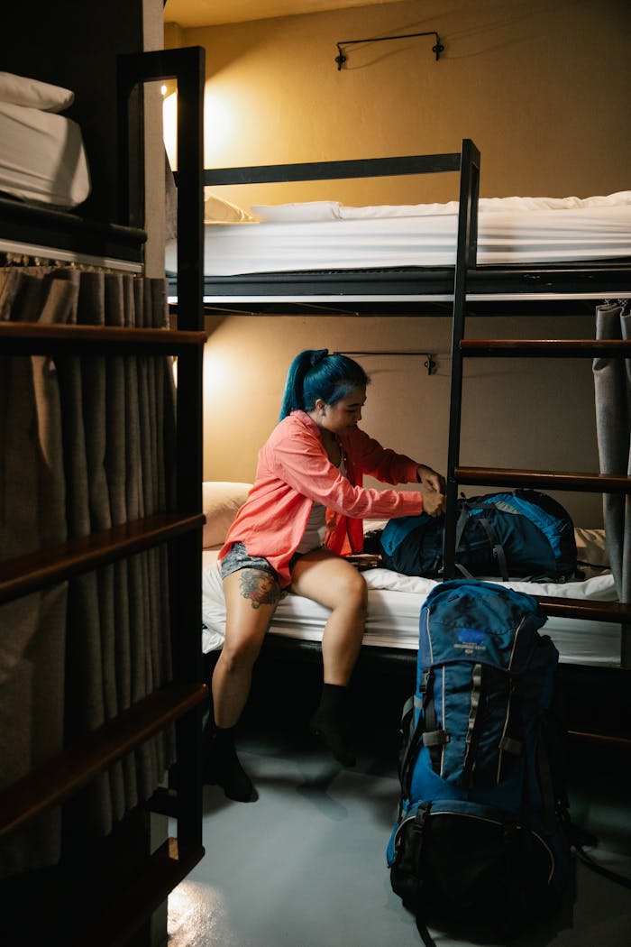 Home Young woman packs her backpack in a cozy hostel room, preparing for travel.