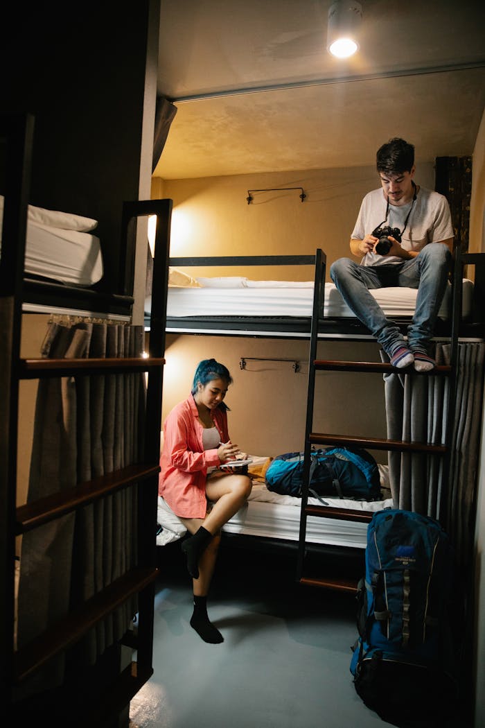 Home Young travelers enjoy downtime in a hostel bunk room, using technology for planning.